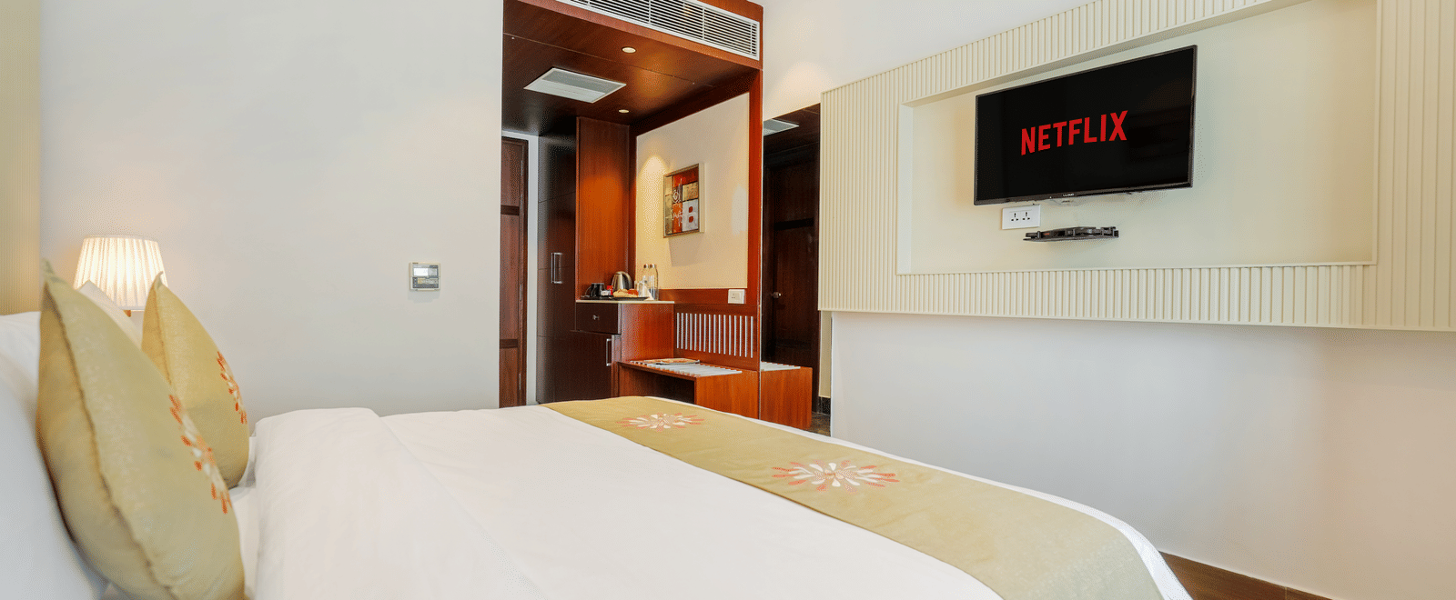A hotel bedroom featuring a bed with a light green runner, a plush headboard, and a wall-mounted television screen at BluSalzz Select City Centre, Amritsar.