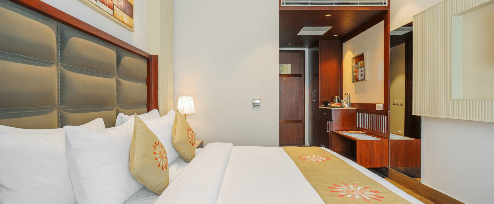 A hotel bed with a dark upholstered headboard, a golden-yellow runner, and a view into the adjacent closet area at BluSalzz Select City Centre, Amritsar.