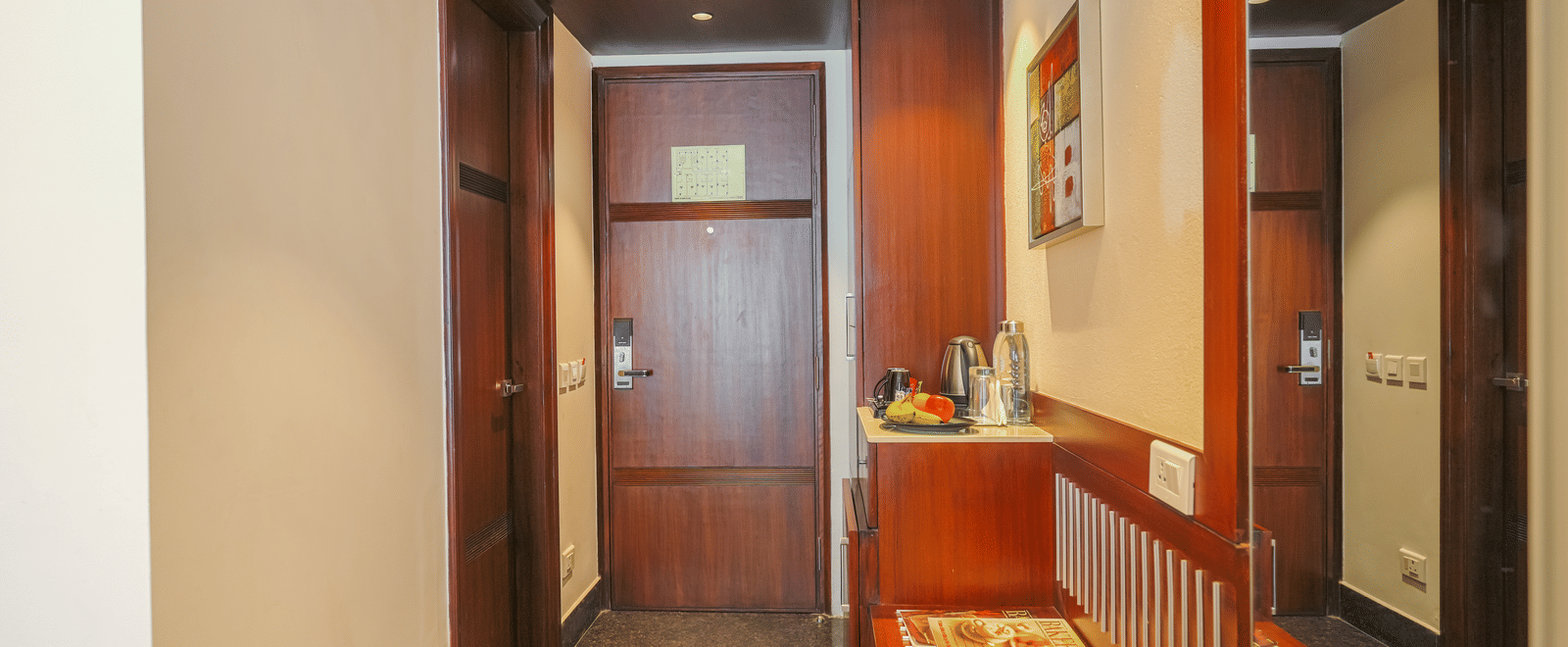 A narrow, wood-panelled hotel room entrance or hallway with a small console table and a dark wooden door at BluSalzz Select City Centre, Amritsar.