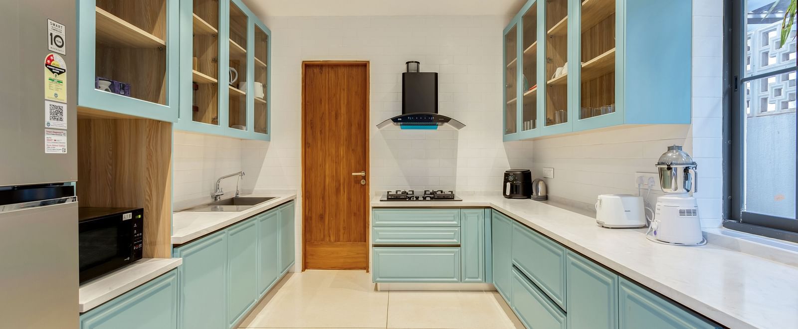 A modern kitchen with pastel blue cabinets, sleek counter tops, and large windows letting in natural light - BluSalzz Villas - Alocassia, Anjuna