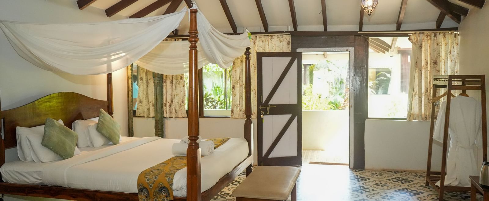 Side view of a spacious room with a large bed, wooden interiors, and a doorway leading outside at De Soul Santé, Morjim.