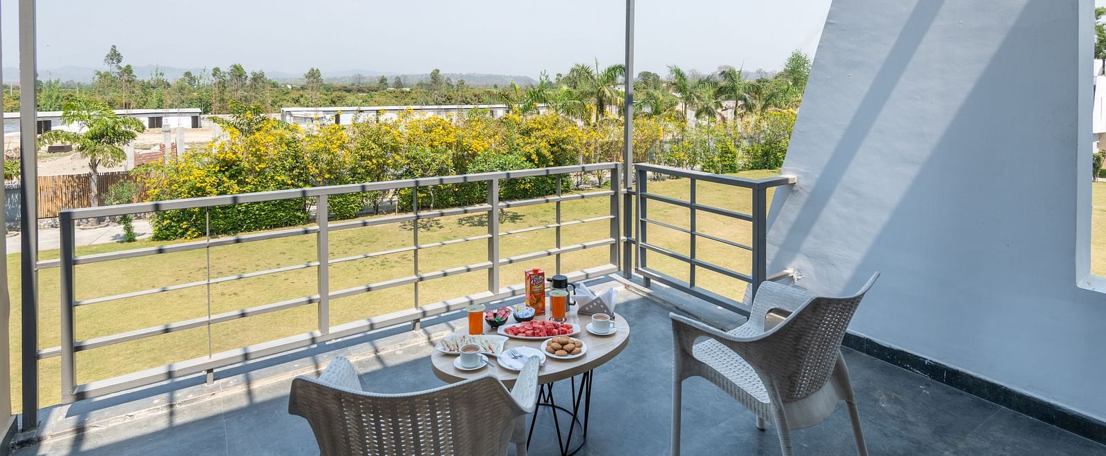 Balcony with chairs and table, offering a view of fields and trees - DLS Forest Vines Resort & Spa, Ramnagar (Jim Corbett)