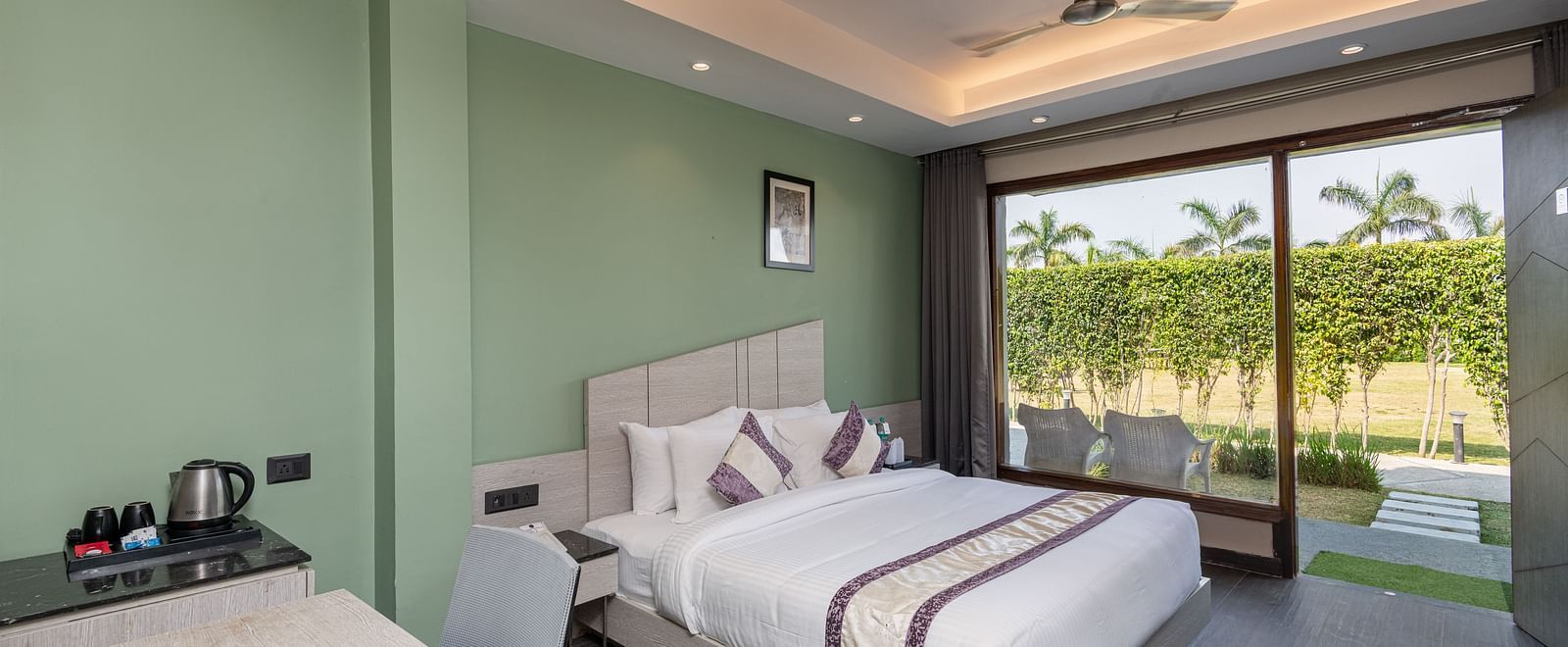 A spacious room at DLS Forest Vines Resort, complete with a large bed, bedside table, table and chairs, and a glass door opening to the balcony.