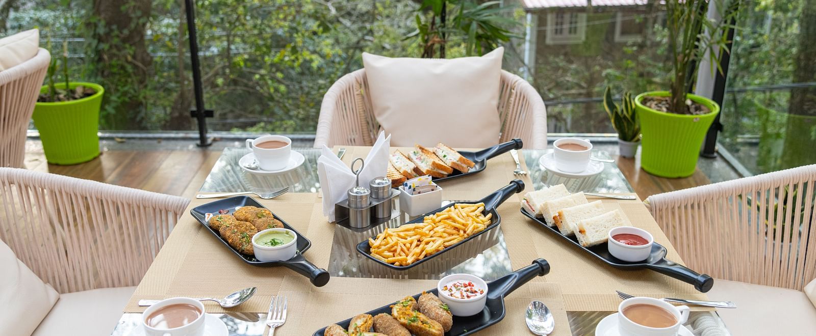 A close up shot of the five food platters laid on a table along with tea cups and the backdrop of trees and greenery - DLS the Emerald, Nainital