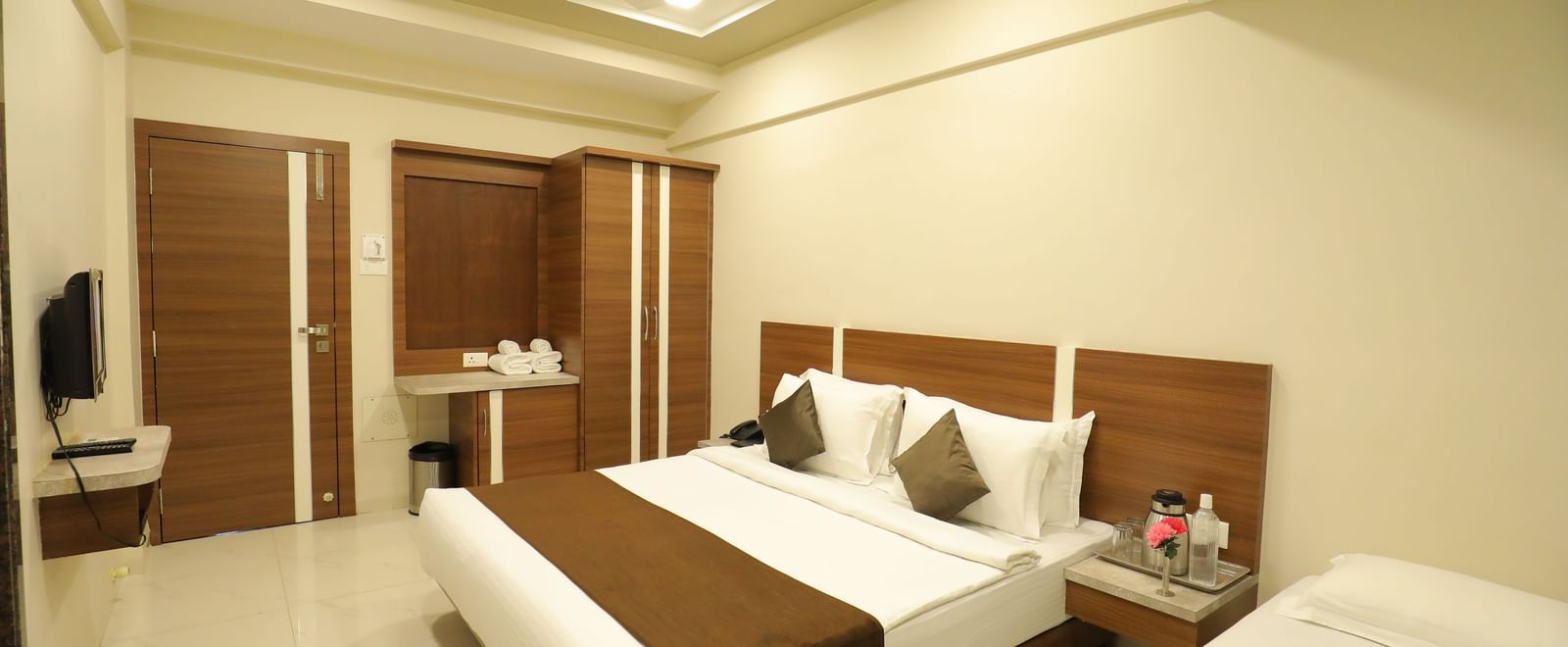 Extended view of the plush queen size bed in the Deluxe Room of the Highland Resort furnished with a wardrobe, wall-mounted TV, and bedside tables.
