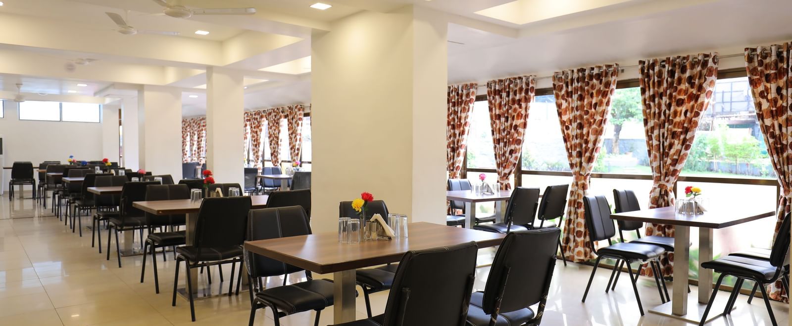 Dining tables in the spacious Darbar Restaurant that has glass windows through which natural light seeps in, at Highland Resort.