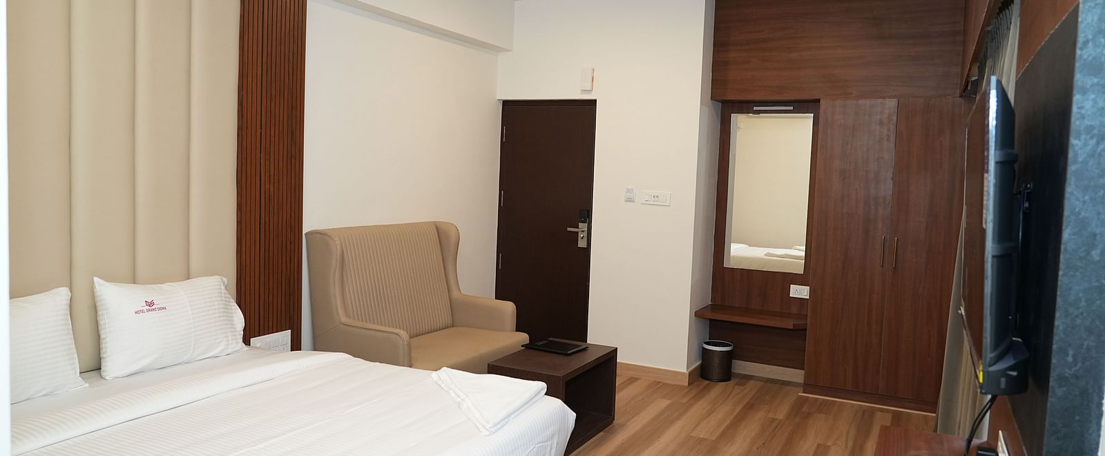 a double bed with a common seating area besides it with a wall mounted television  in the room - Hotel Grand Sigma