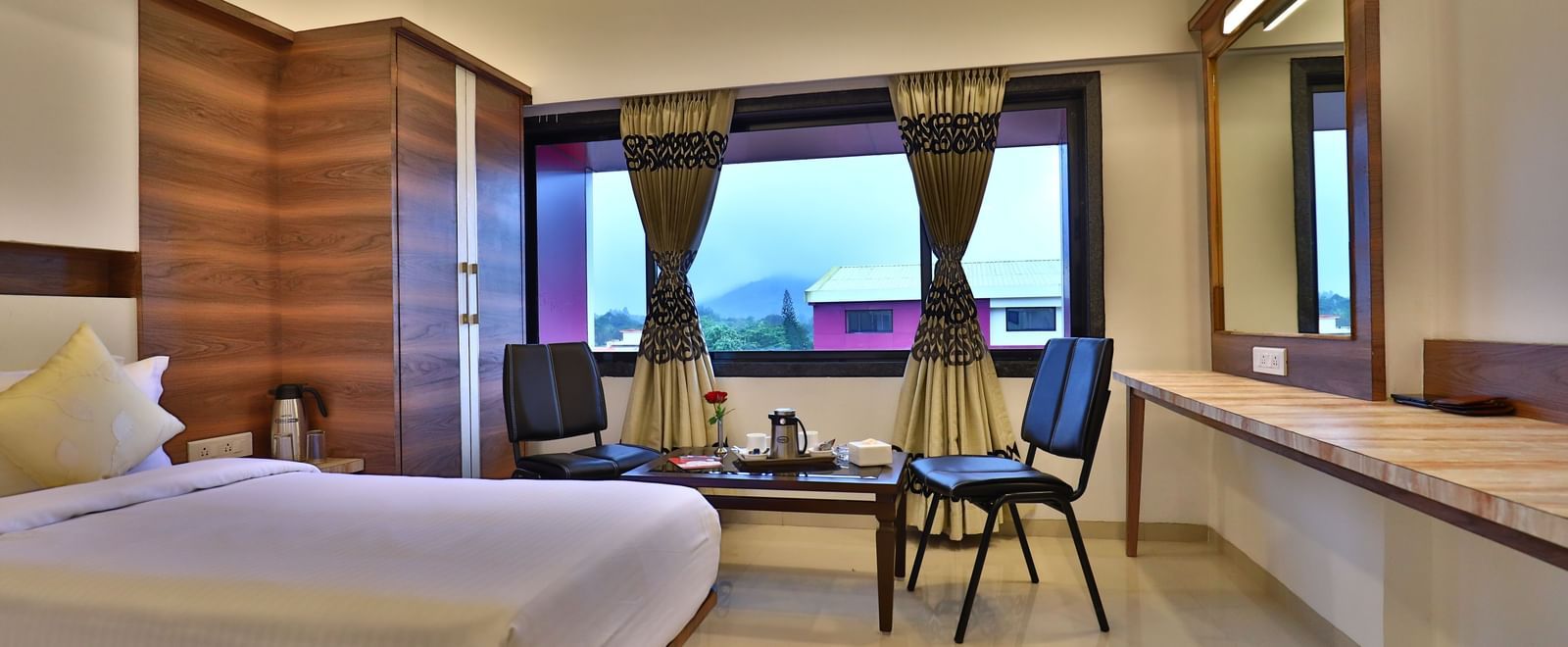 A bedroom at Imperial Grande with a bed, a chair, and a table, with a window showing a view outside.