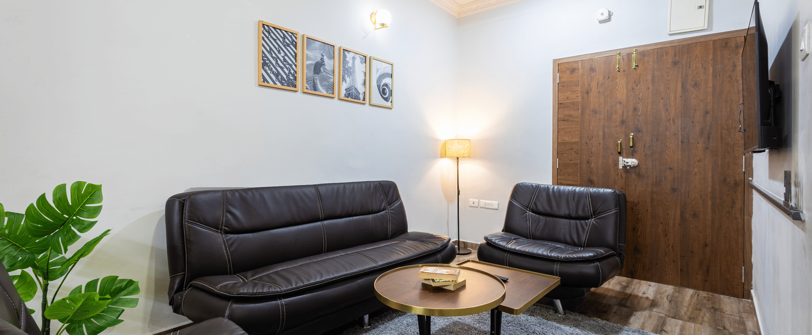 The separate living room of the 4BHK of Kove Smart Stays, featuring upholstered sofas with a centre table placed on a carpet in the well-lit room.
