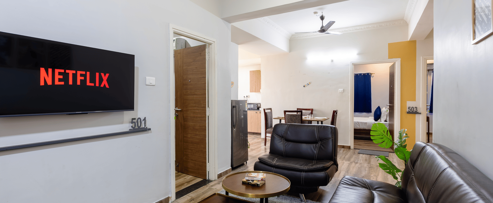 The living area in the separate living room of the 4BHK of Kove Smart Stays, seen with the multiple sofas facing the wall-mounted television.