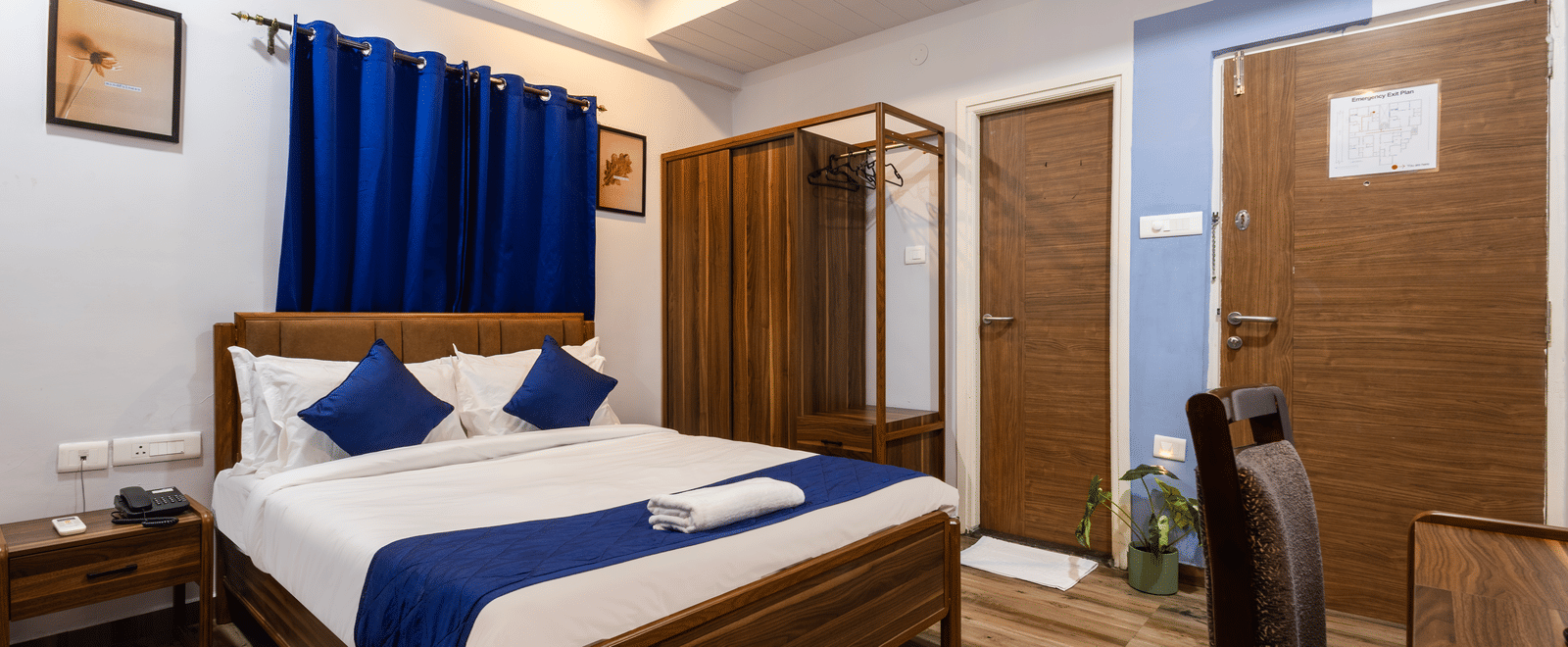 A bedroom in the 4BHK of Kove Smart Stays, seen with wooden flooring, a queen size bed, a wooden wardrobe, and ample overhead lighting.