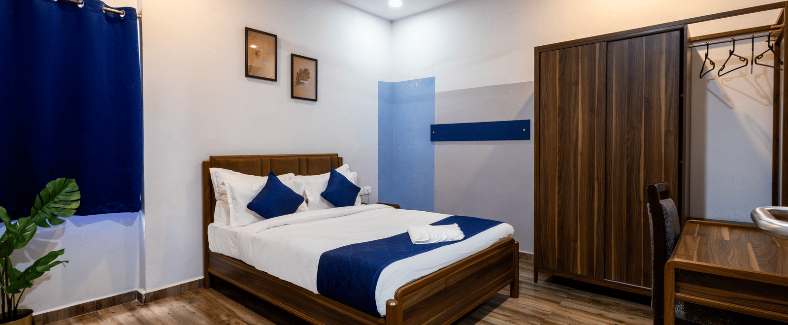 A bedroom in the 4BHK of Kove Smart Stays, seen with wooden flooring, a queen size bed, a wooden wardrobe, and ample overhead lighting.