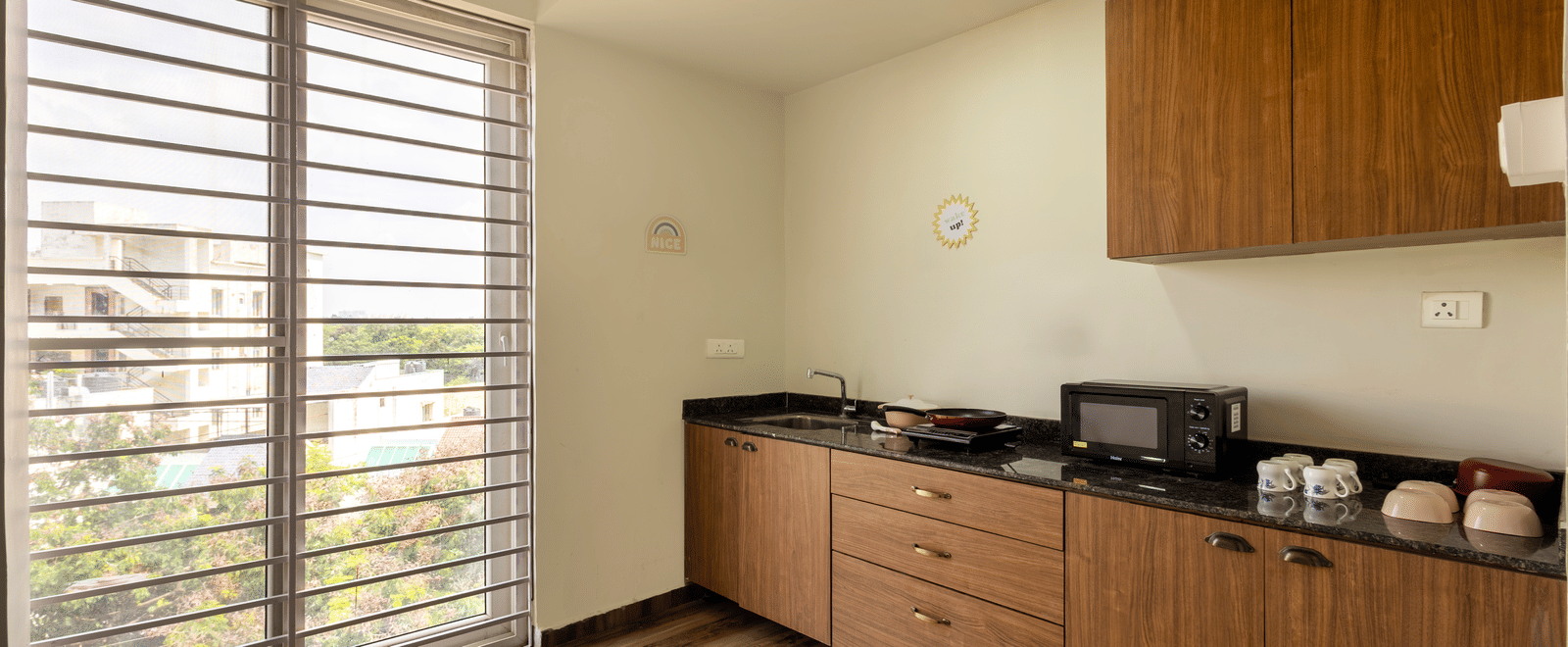 The kitchen of the 4BHK of Kove Smart Stays featuring wooden cabinets, an oven placed on the marble counter alongside cutlery and a sink.