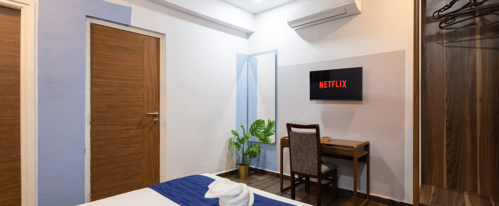 Deluxe Room seen from a corner of the room highlighting the bed facing the wall-mounted TV and work desk.