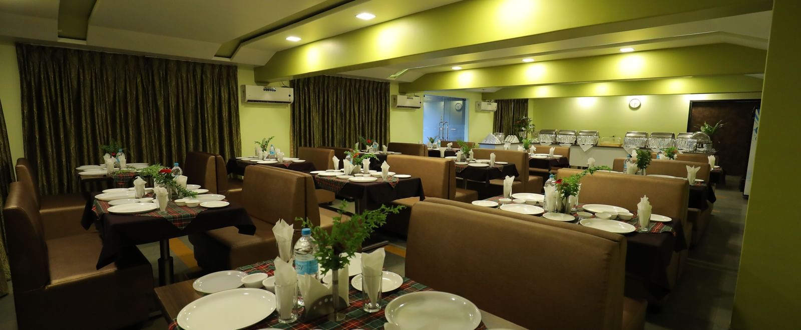 Dining area with neatly arranged tables and chairs at Krushnai Resort, with plates and cutlery placed.