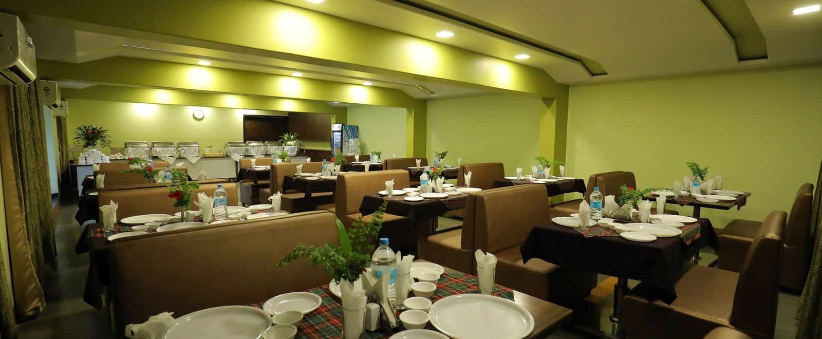 Dining setup at Krushnai Resort with round tables and brown chairs, plates and glasses on the table.