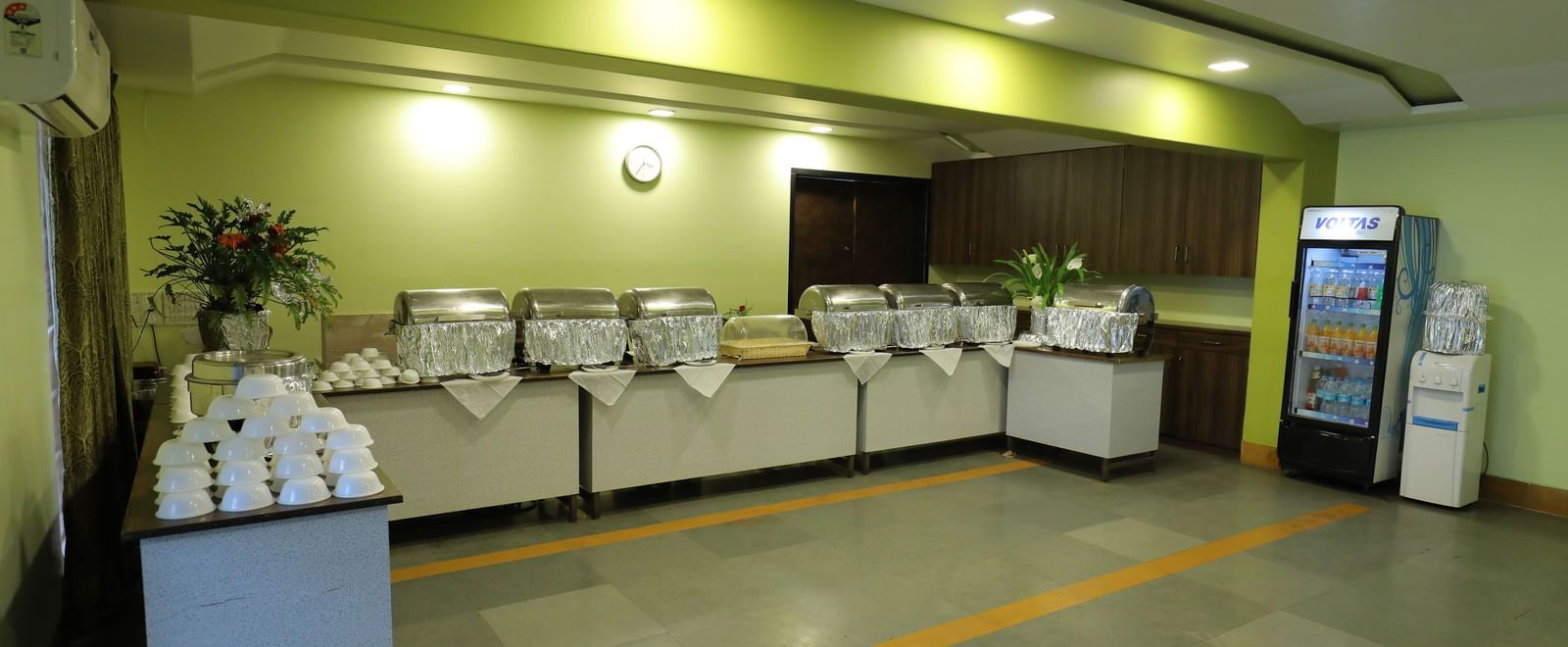 Buffet counter at Krushnai Resort with white dishes stacked and a beverage refrigerator in the background.