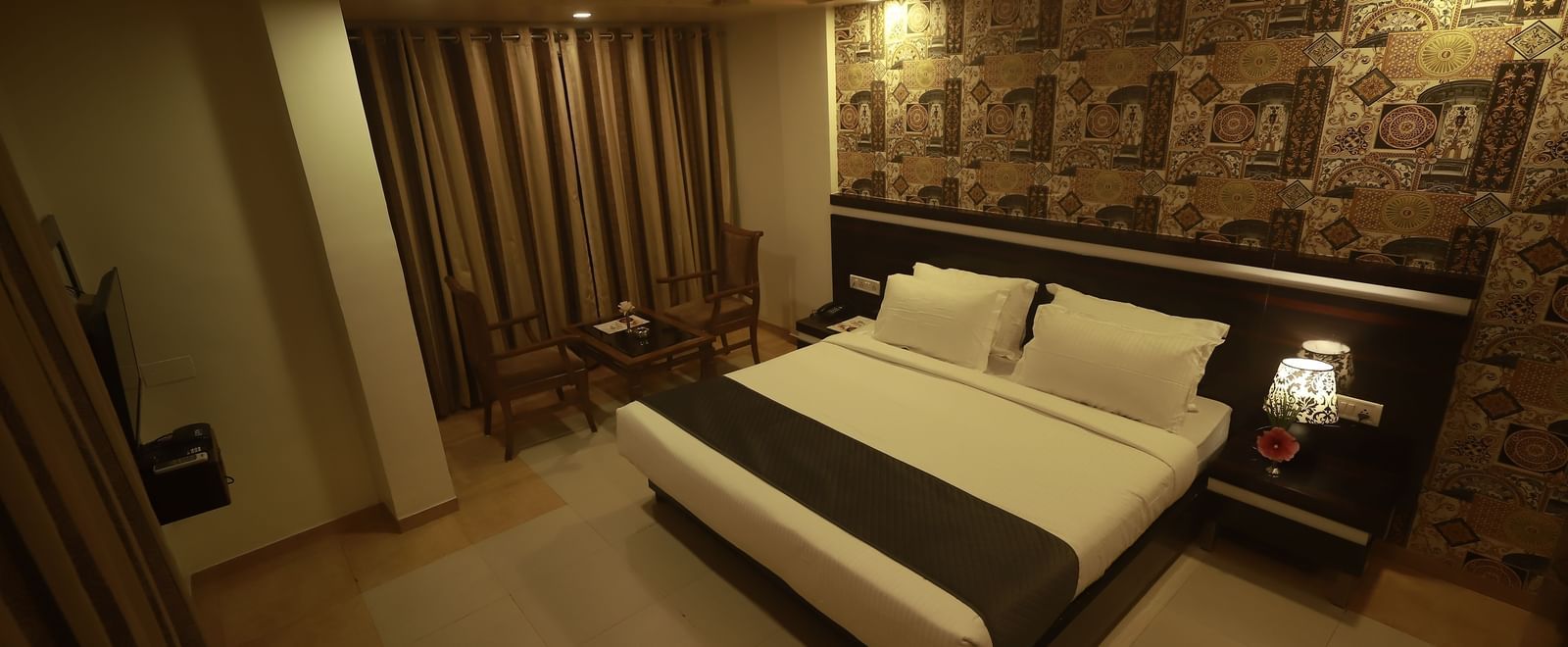A Deluxe Room of Mountview Resort furnished with a king size bed, a wall-mounted TV, bedside tables, and a seating area in front of closed curtains.
