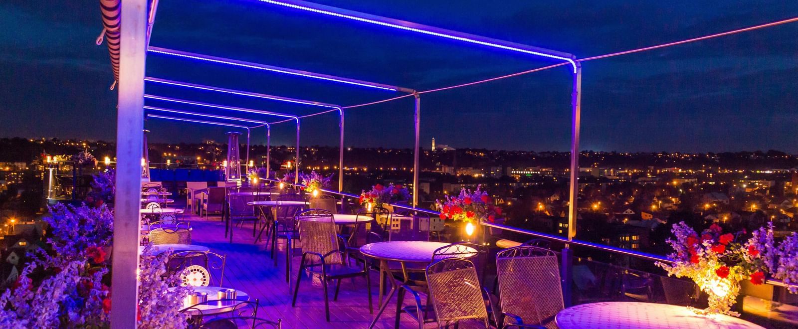 A rooftop terrace bar at night with glowing neon lights and outdoor seating.