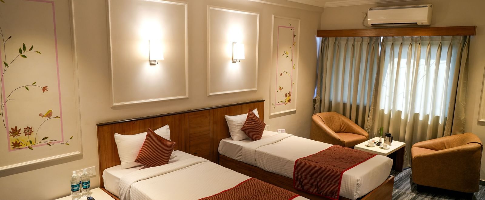 Comfortable twin room with two neatly arranged beds and cosy seating at Pravasa Hotel Kolhapur.