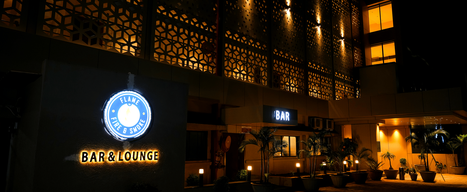 The striking exterior facade of Pravasa Hotel, Kolhapur, is illuminated at night, highlighting the modern geometric screen design.