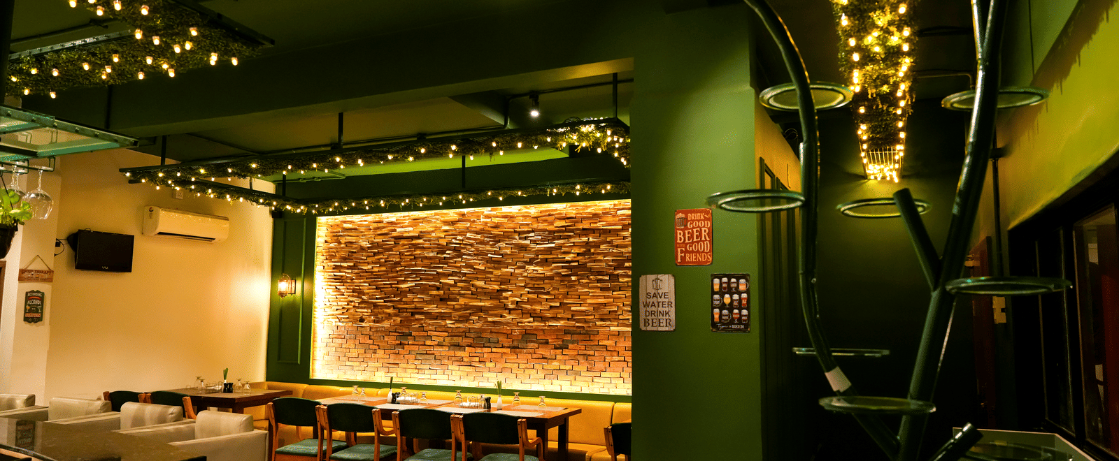 A vibrant lounge area with striking green walls, comfy seating, and a feature wall of exposed brick at Pravasa Hotel, Kolhapur.