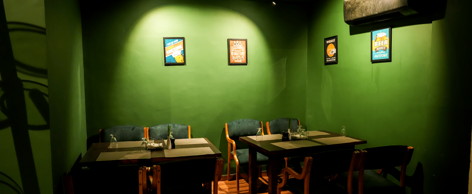  A private or cosy dining room with dark tables, green walls, and framed artwork at Pravasa Hotel, Kolhapur.