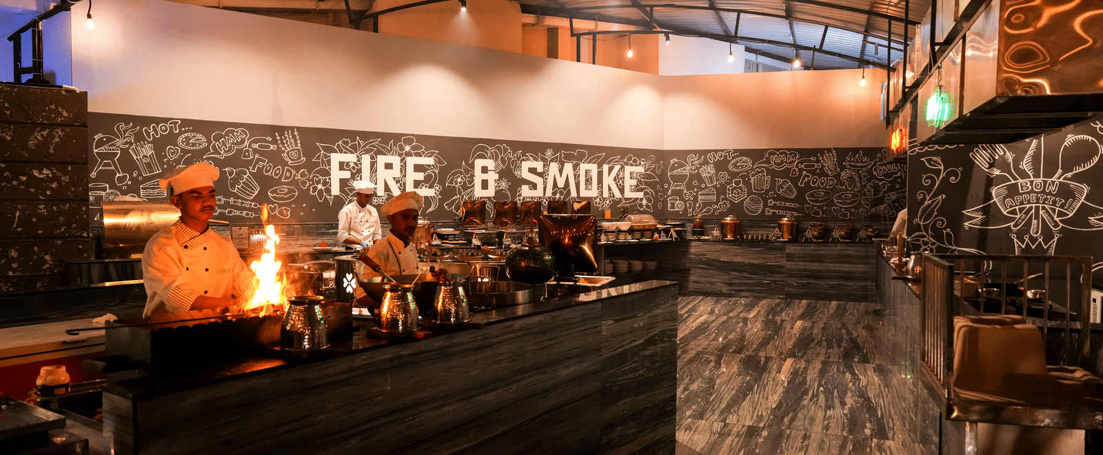 Chefs cooking in open kitchen area with visible flames at Pravasa Hotel, Kolhapur.