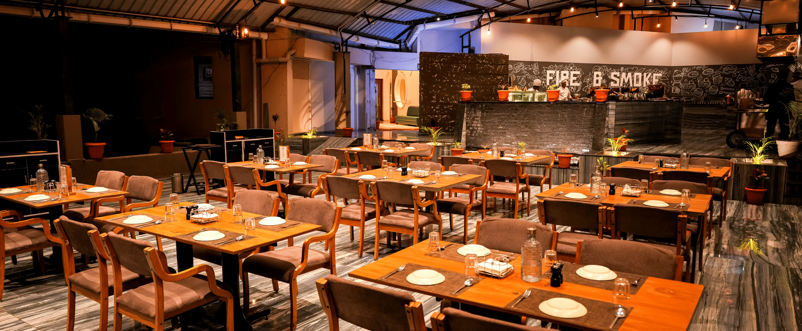 Dining area with tables and chairs under indoor lighting at Pravasa Hotel, Kolhapur.