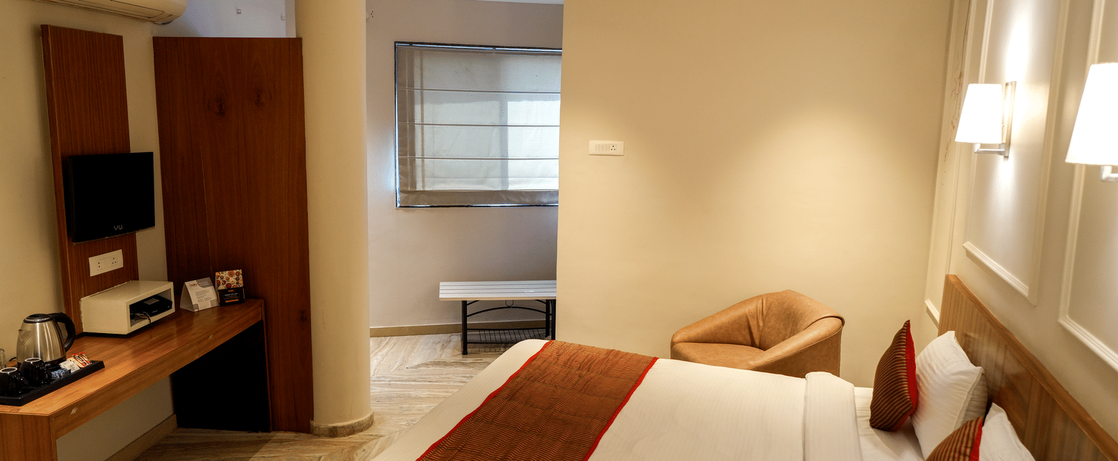  A well-equipped guest room with a wooden desk, a kettle, and a separate sitting area near a window at Pravasa Hotel, Kolhapur. 