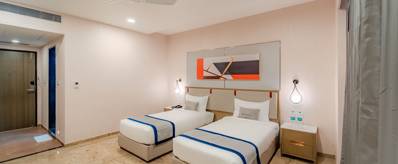Twin beds with white and blue bedding in a well-lit hotel room | Superior Room | Pravasa Hotel, Vijayapura