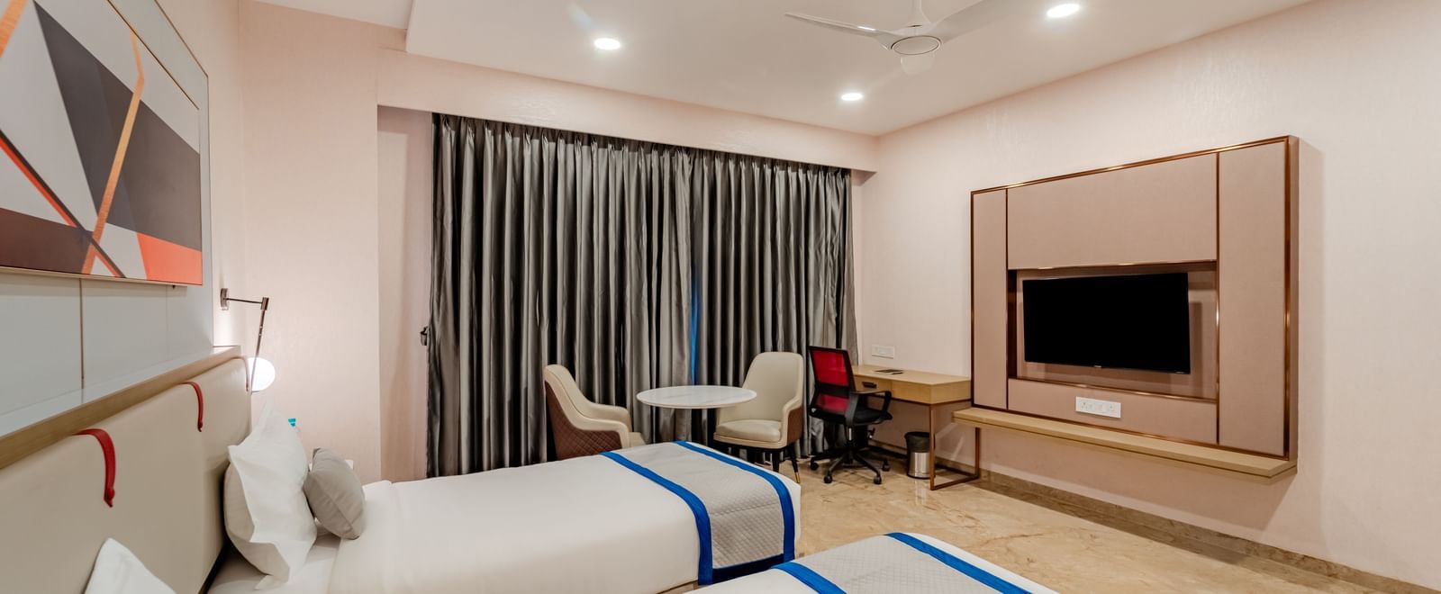 Corner of a hotel room featuring twin beds and a wall-mounted TV | Superior Room | Pravasa Hotel, Vijayapura