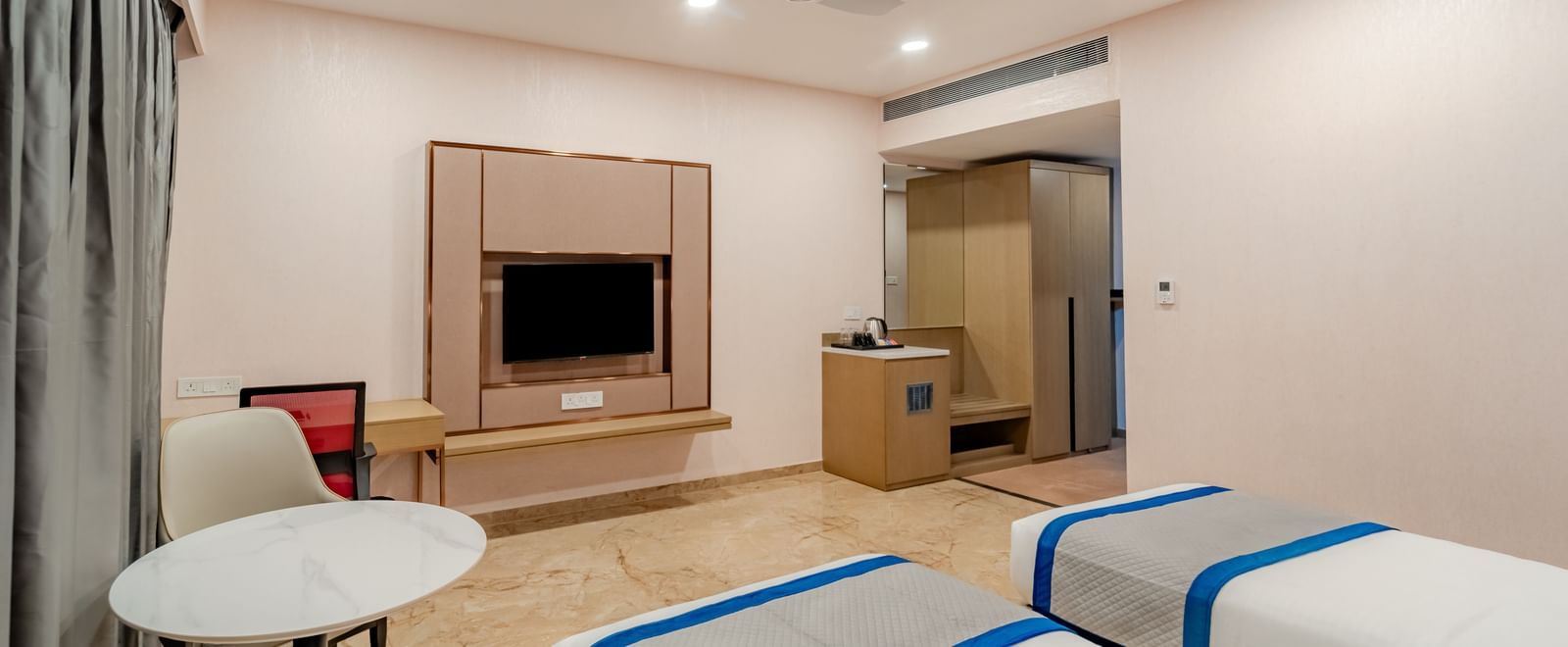 A hotel room featuring twin beds and a wall-mounted TV | Superior Room | Pravasa Hotel, Vijayapura