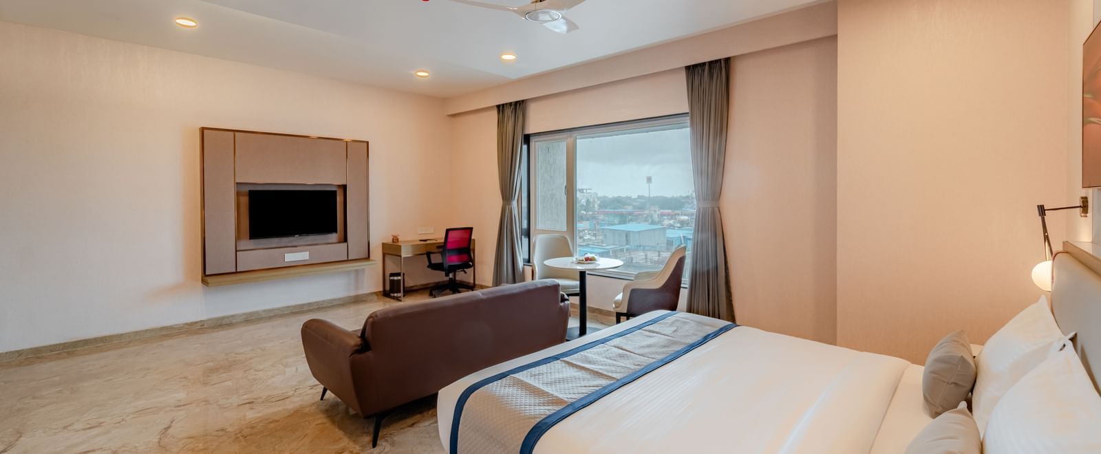  A spacious room with a king-size bed, a sofa, and a wall-mounted television | Studio Suite | Pravasa Hotel, Vijayapura