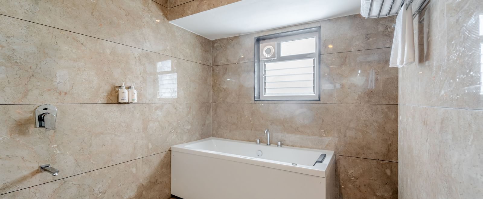 A suite bathroom with a white bathtub and patterned beige tiles | Suite | Pravasa Hotel, Vijayapura
