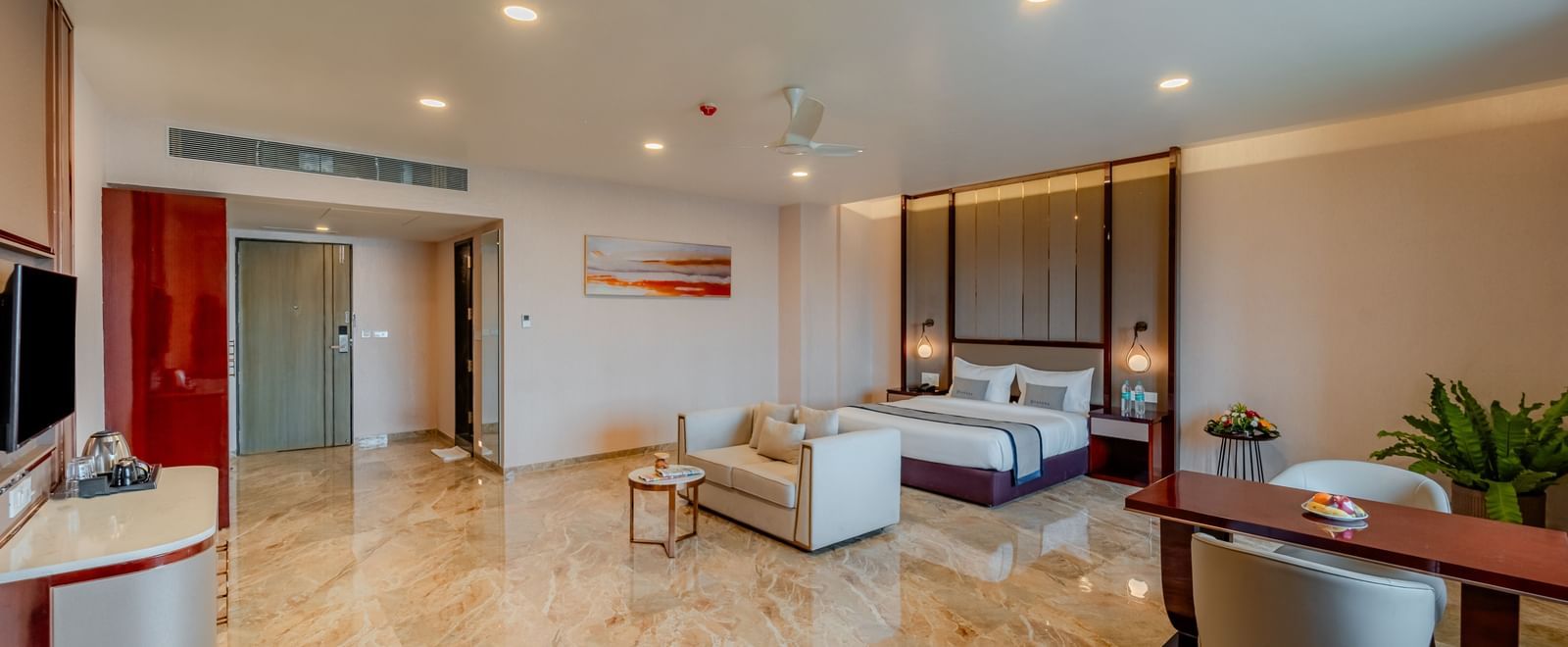 A bright and elegant suite with a bed, living space, and a dining setup | Suite | Pravasa Hotel, Vijayapura