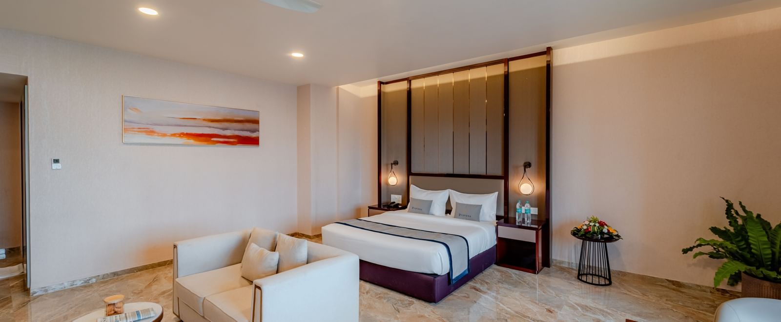 Bright and elegant suite with a bed, living space, and a dining setup | Suite | Pravasa Hotel, Vijayapura