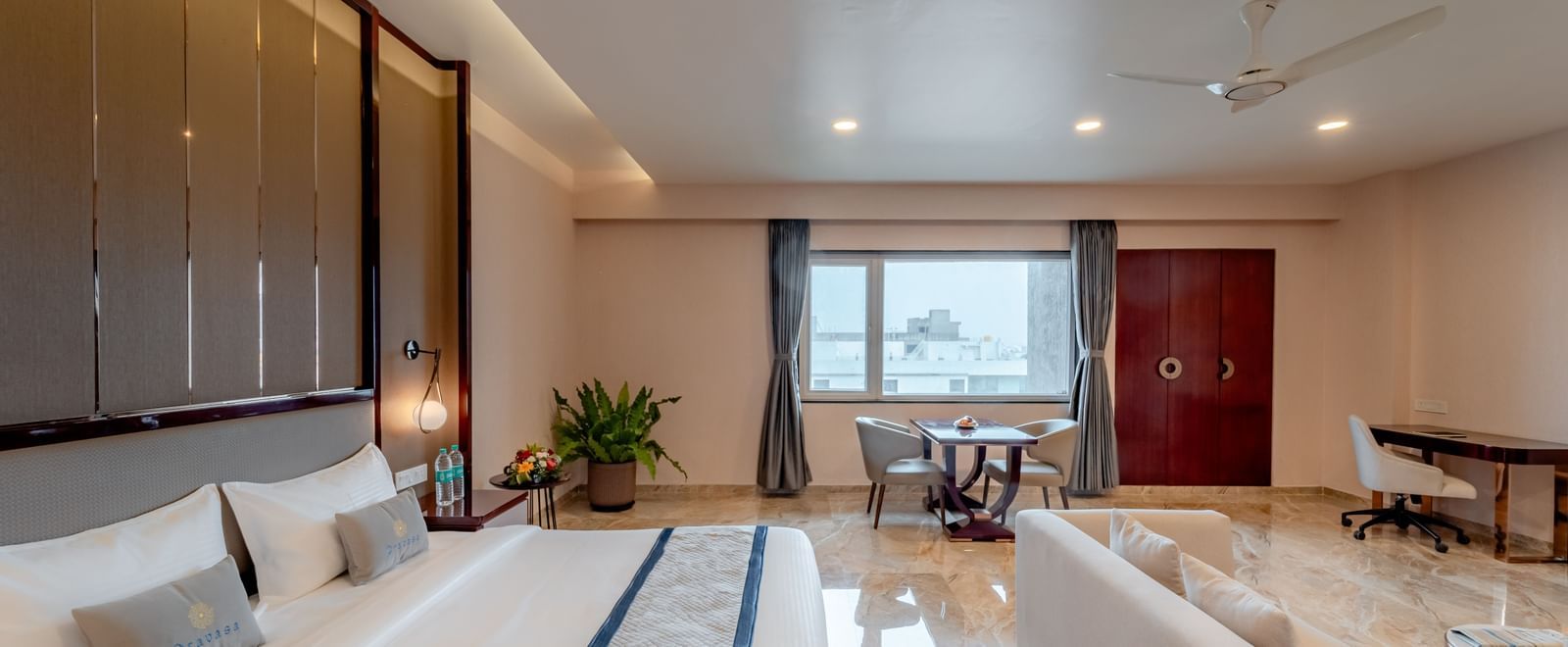 A apacious suite featuring a comfortable bed, lounge area, and city views | Suite | Pravasa Hotel, Vijayapura