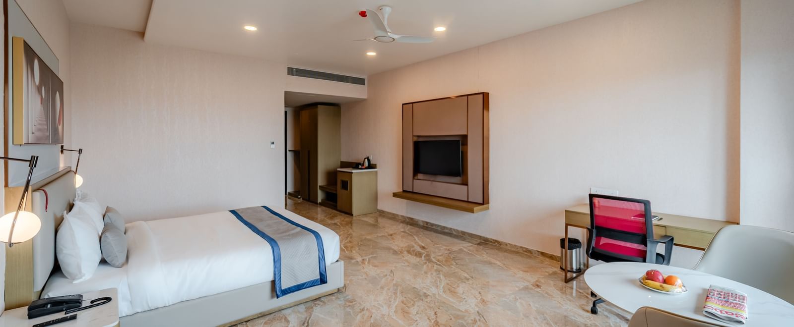  A hotel bedroom with a large bed, TV, and a desk, well-lit | Premium Room | Pravasa Hotel, Vijayapura