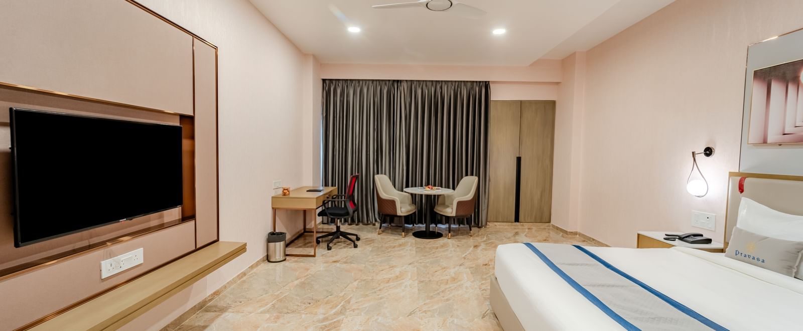 Well-appointed hotel room with a king bed, flat-screen TV, and seating area | Premium Room | Pravasa Hotel, Vijayapura