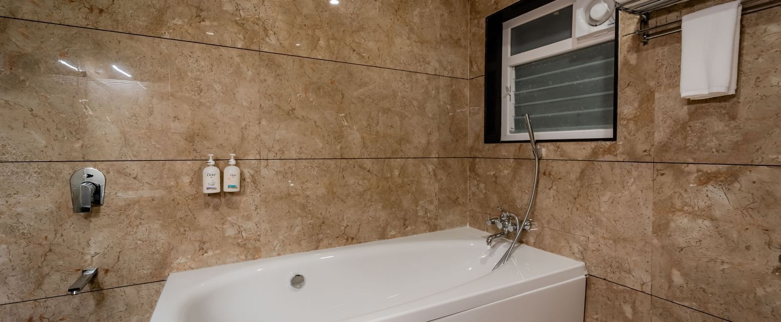 Close-up of a white bathtub in a marble-tiled bathroom | Premium Room | Pravasa Hotel, Vijayapura