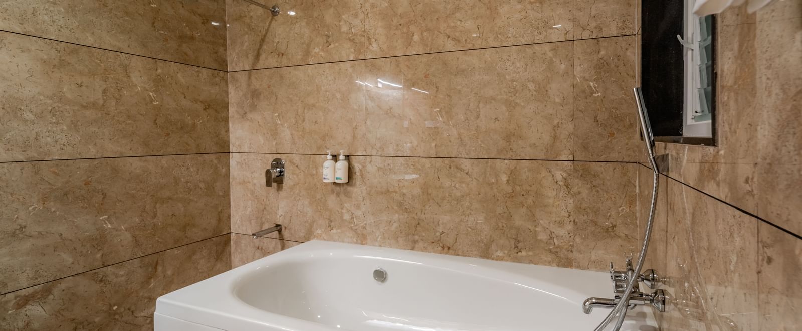 Modern bathroom with a clean white bathtub and marble-patterned tiles | Premium Room | Pravasa Hotel, Vijayapura