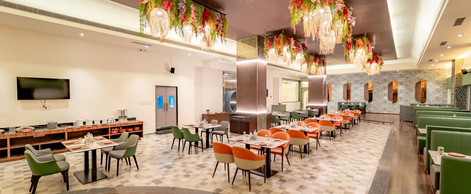 A rstaurant space with orange and green seating and intricate ceiling decorations | Pravasa Hotel, Vijayapura