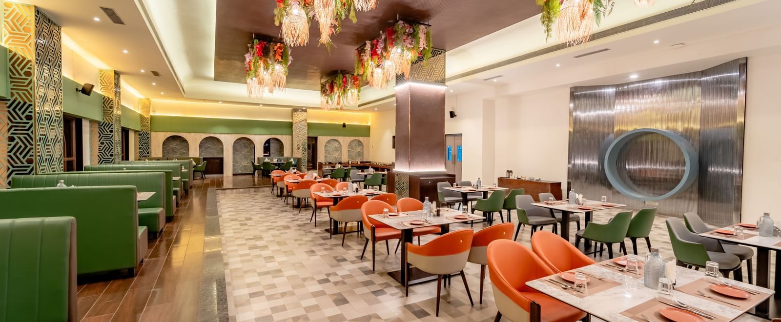Dining area with green sofas and orange chairs and decorative hanging elements | Pravasa Hotel, Vijayapura