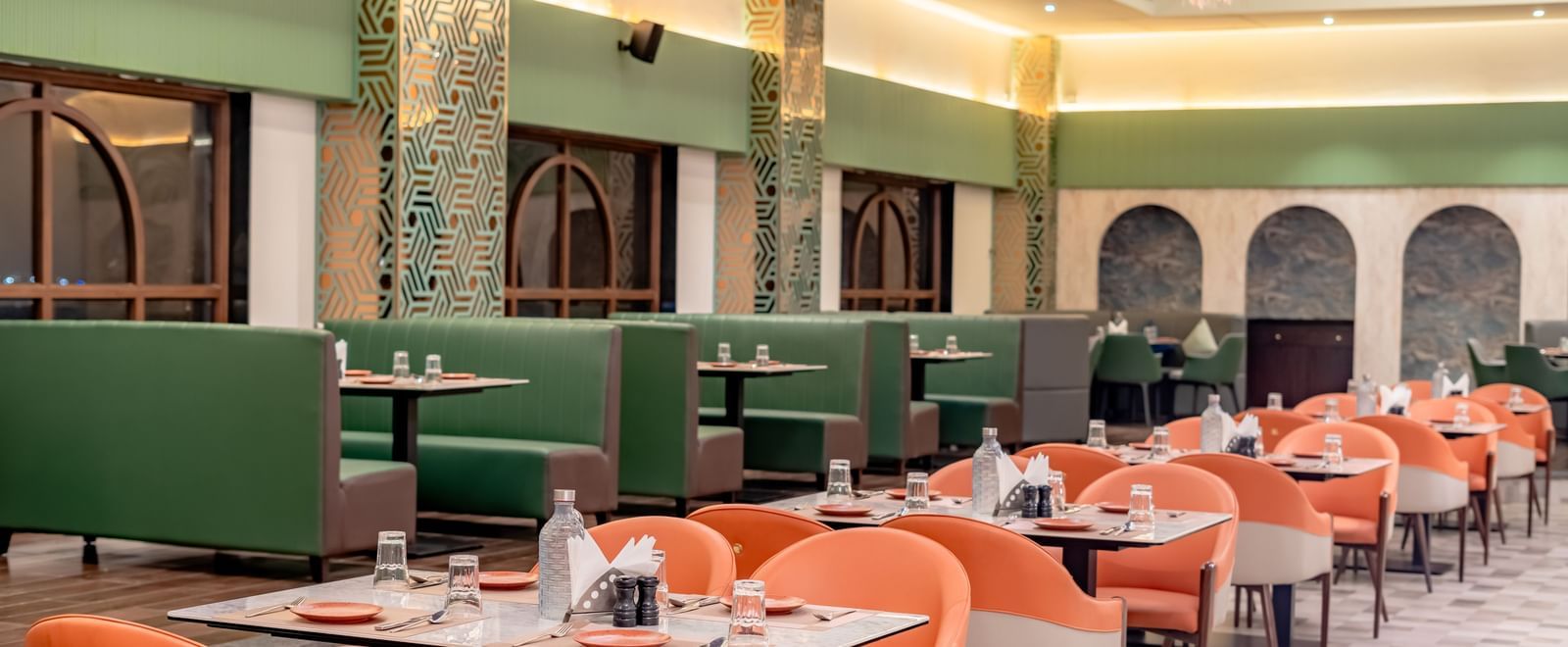 A dining area with green and orange chairs and decorative hanging elements | Pravasa Hotel, Vijayapura