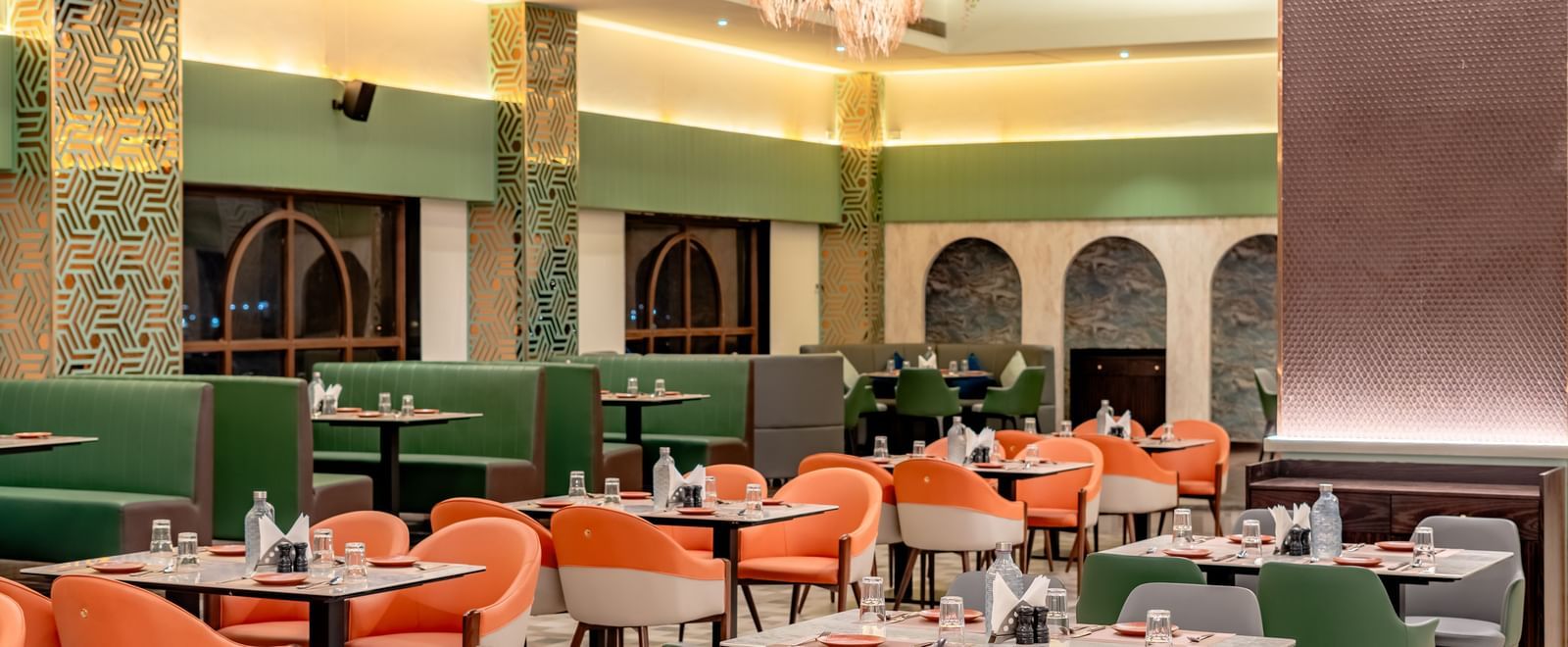 Dining area with green and orange chairs and decorative hanging elements | Pravasa Hotel, Vijayapura