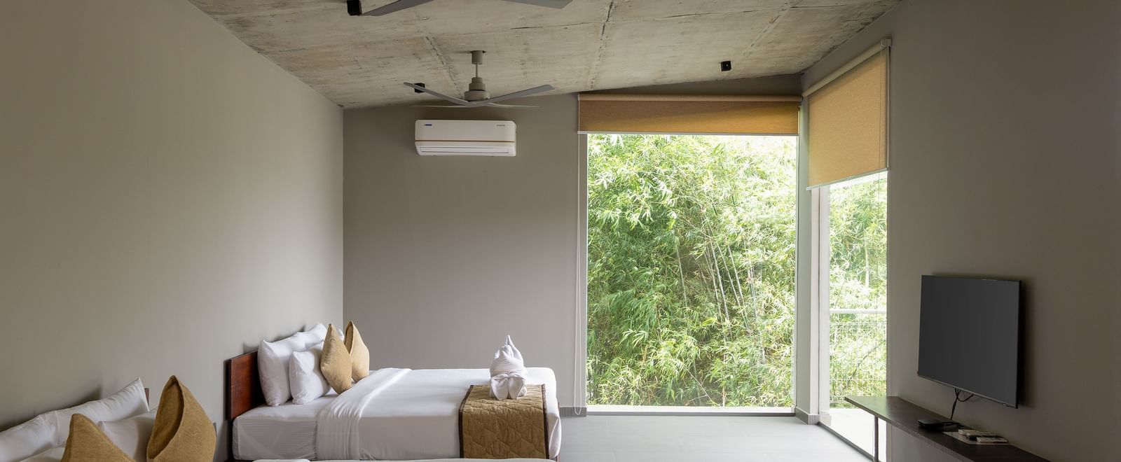 A bedroom with a large bed, a ceiling fan, a television, and a panoramic view of the outdoors through a large window | Gaia Studio | RD's Nature Retreat, Bangalore