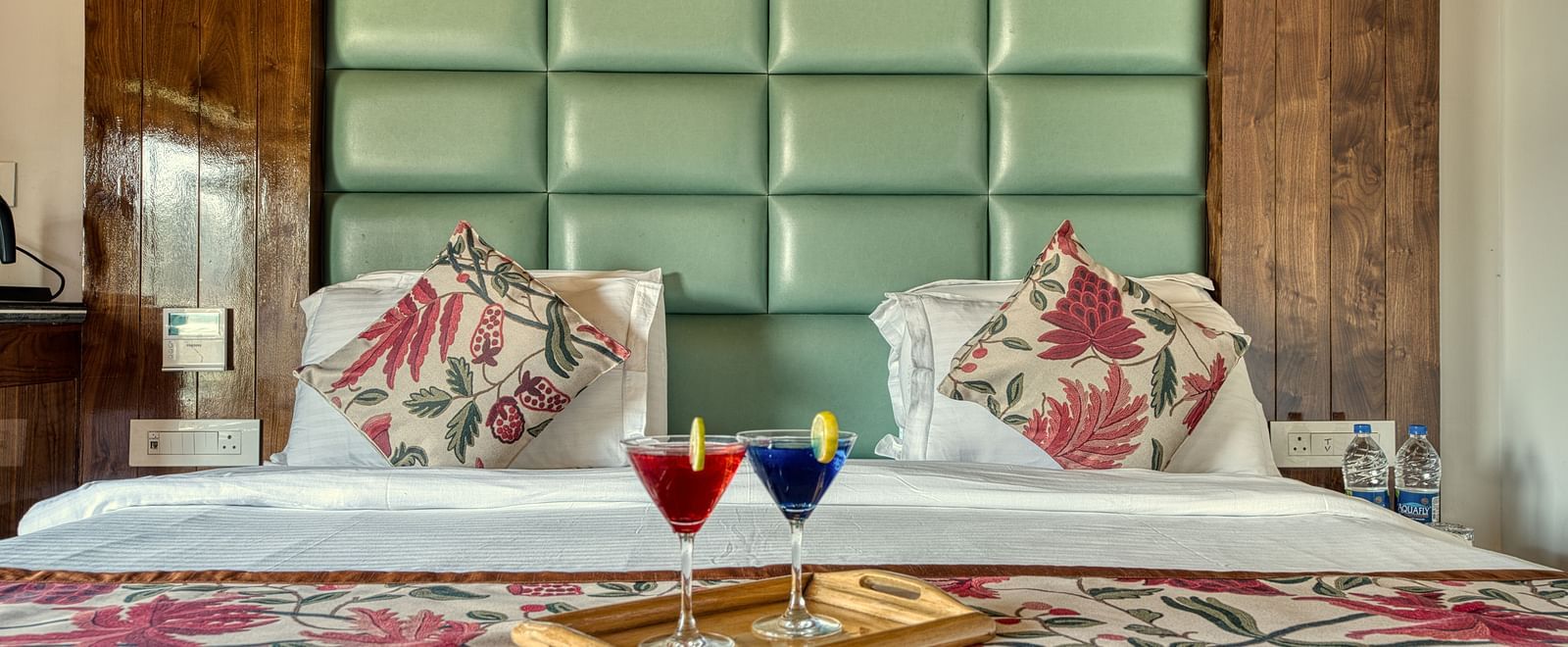 King size bed with floral linen and twin welcome drinks at Royal Comfort Regency, crafted for indulgent rest and relaxation.