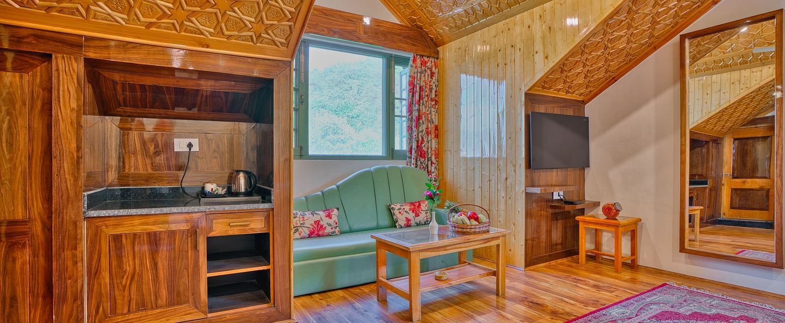 Interior of a room at Royal Comfort Regency showing a wooden kitchenette, seating area, sloped ceiling and large window with natural light.
