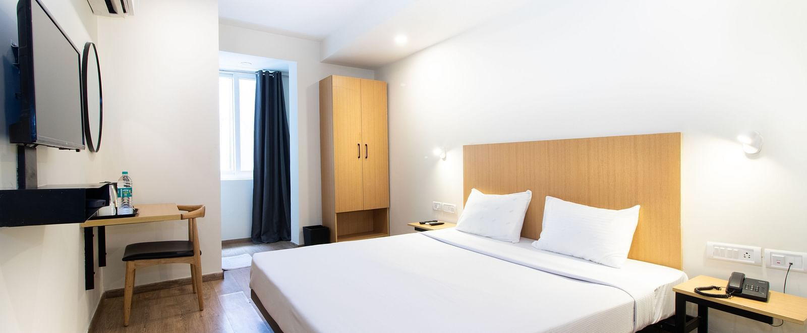 A bedroom with a double bed, white bedding, a bedside table, and a visible doorway - Sanctum Suites Richmond Road, Bangalore